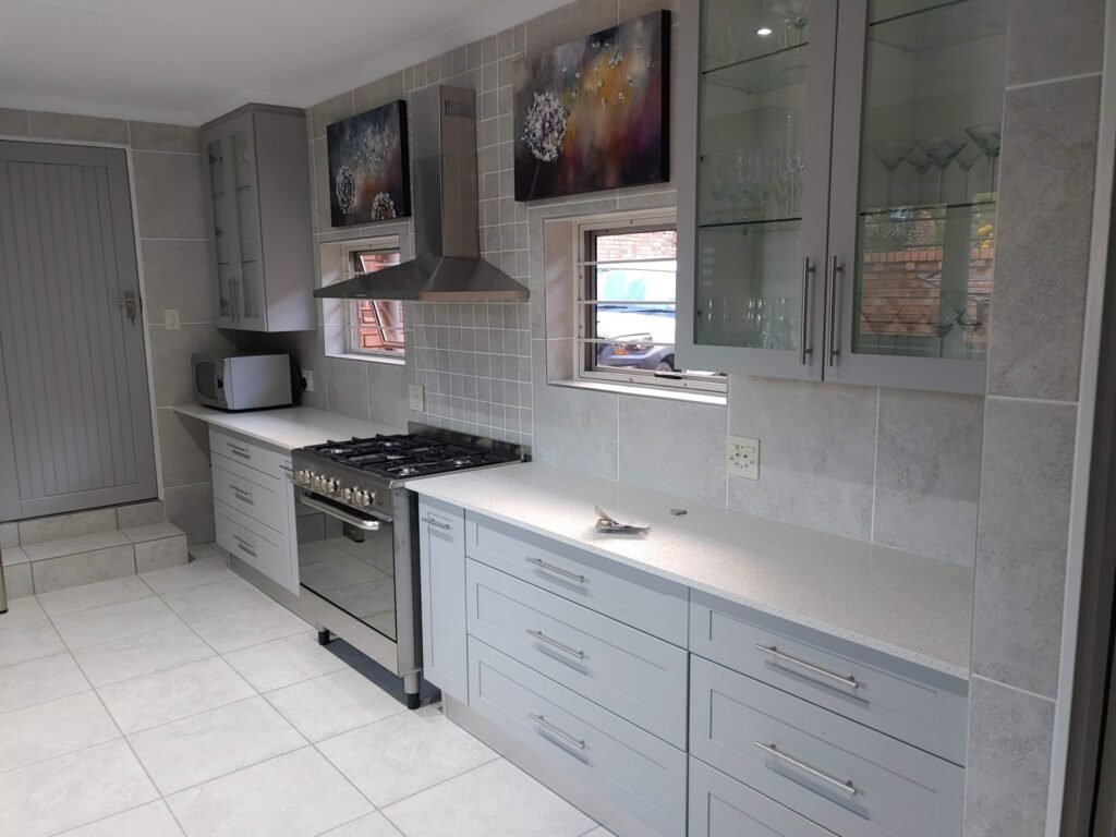 Light grey shaker-style kitchen with stainless appliances and quartz tops