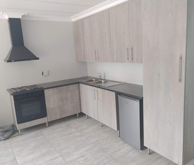 Compact modern L-shaped kitchen with grey wood-grain cabinets and dark tops